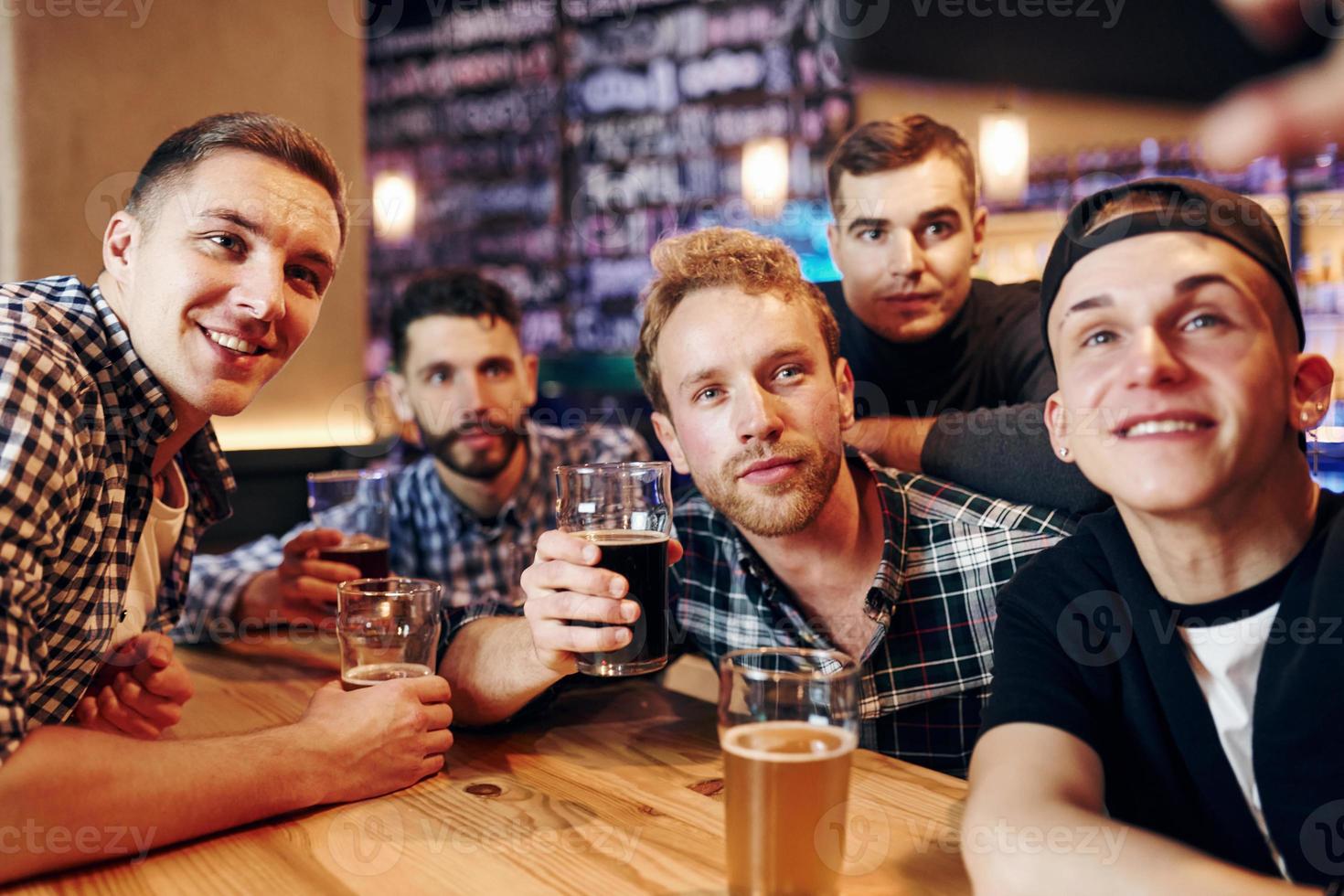 Man takes selfie by phone. Group of people together indoors in the pub have fun at weekend time photo