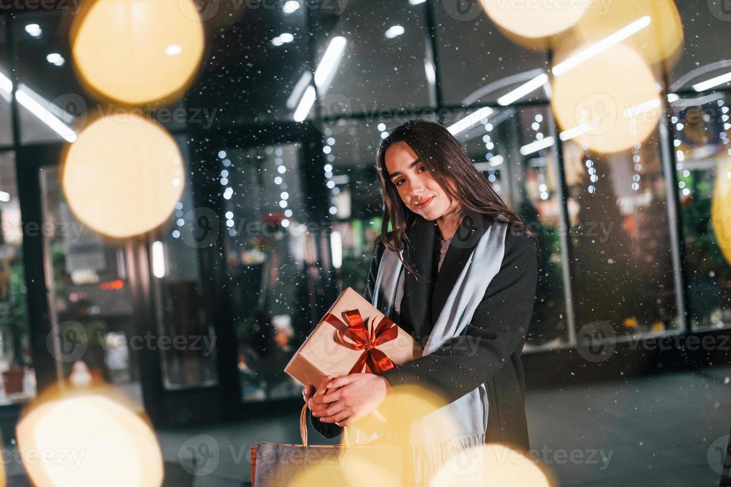 From the shop with gift box in hands. Cheerful woman is outdoors at Christmas holidays time. Conception of new year photo