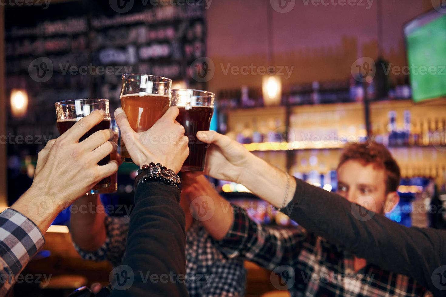 Cheering by knocking beer glasses. Group of people together indoors in the pub have fun at weekend time photo