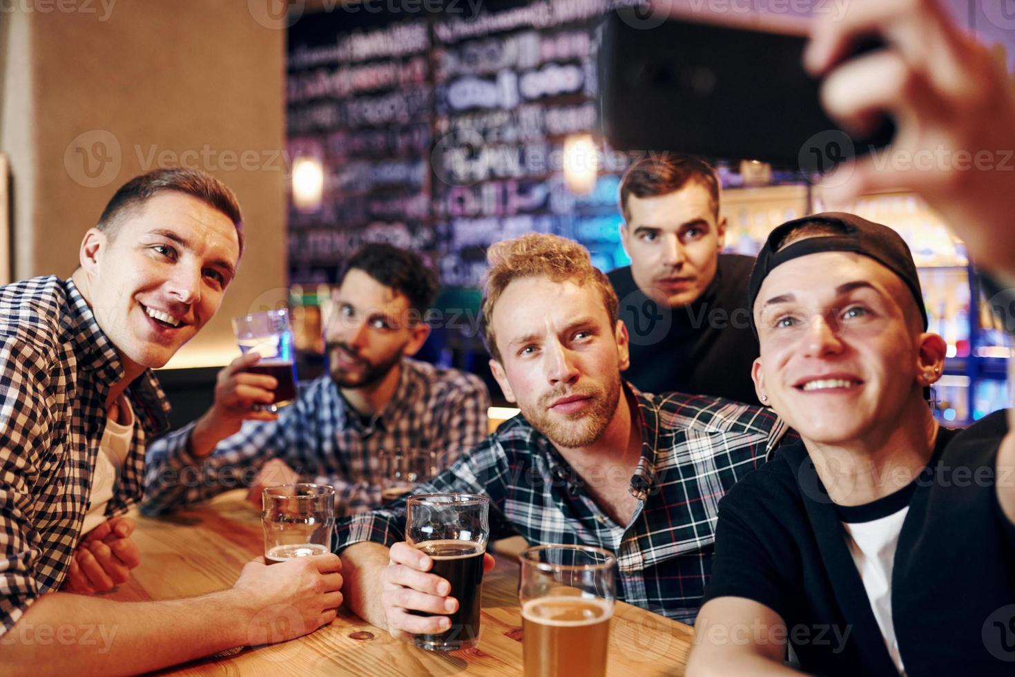 Man takes selfie by phone. Group of people together indoors in the pub have fun at weekend time photo