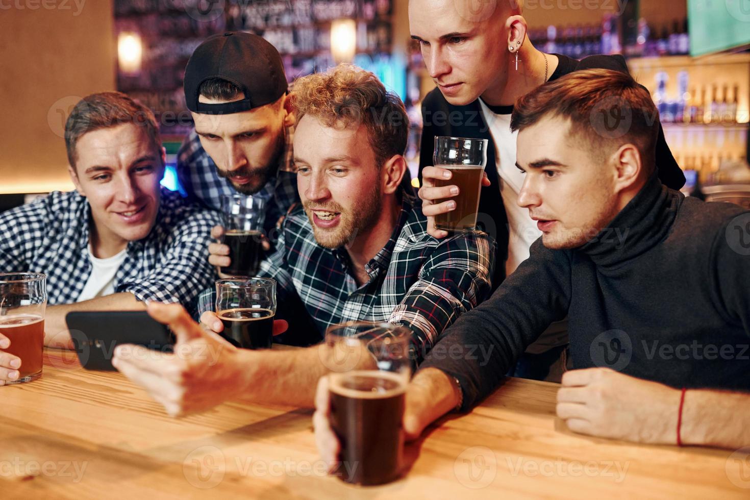 Uses phone. Group of people together indoors in the pub have fun at weekend time photo