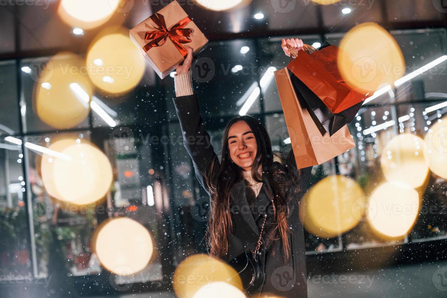 From the shop with gift box in hands. Cheerful woman is outdoors at Christmas holidays time. Conception of new year photo