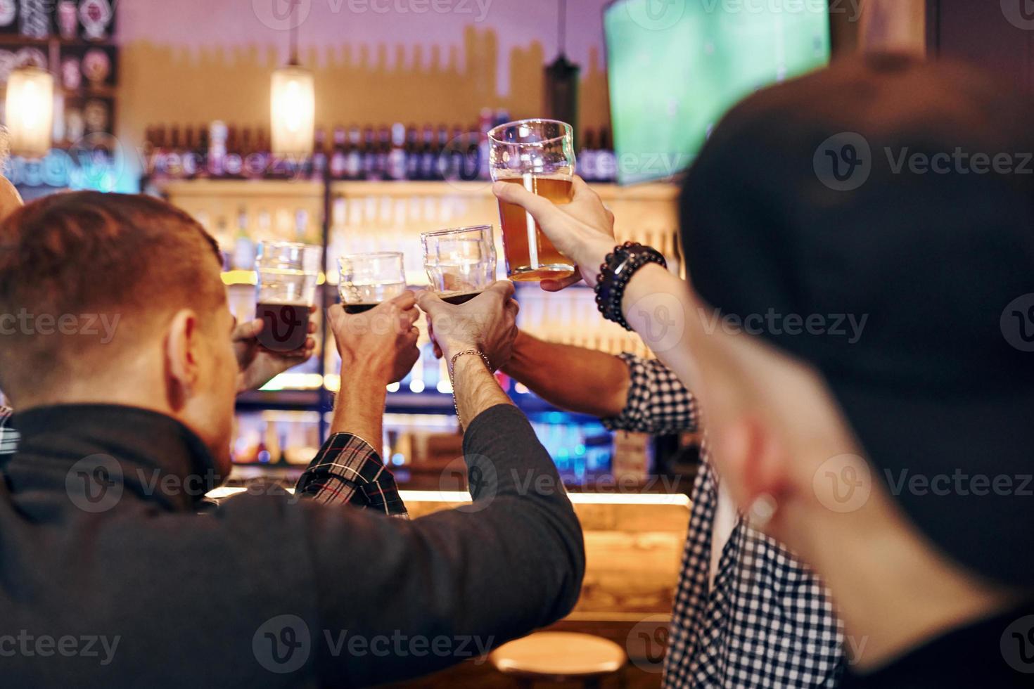 Cheering by knocking beer glasses. Group of people together indoors in the pub have fun at weekend time photo