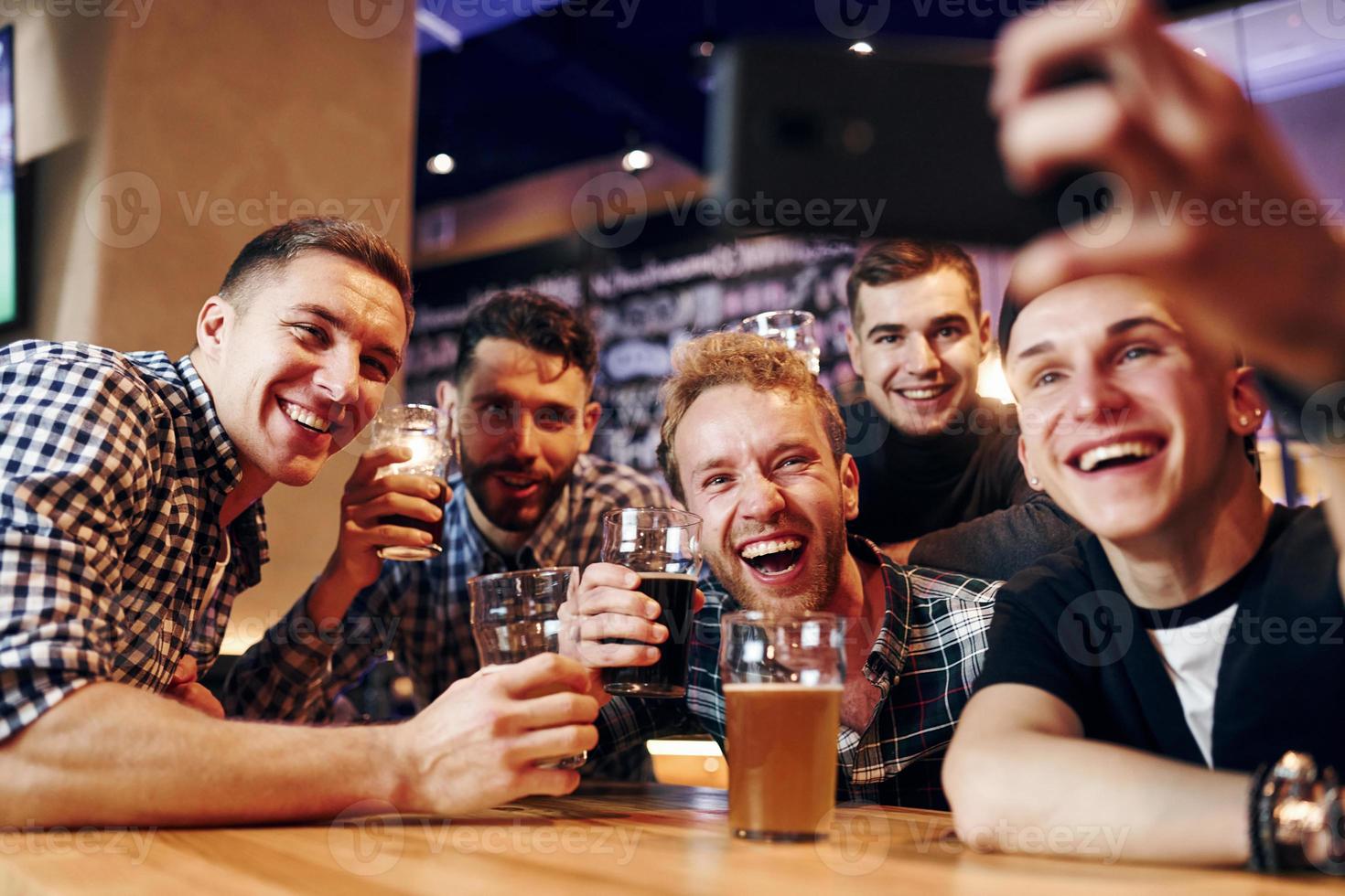 Man takes selfie by phone. Group of people together indoors in the pub have fun at weekend time photo