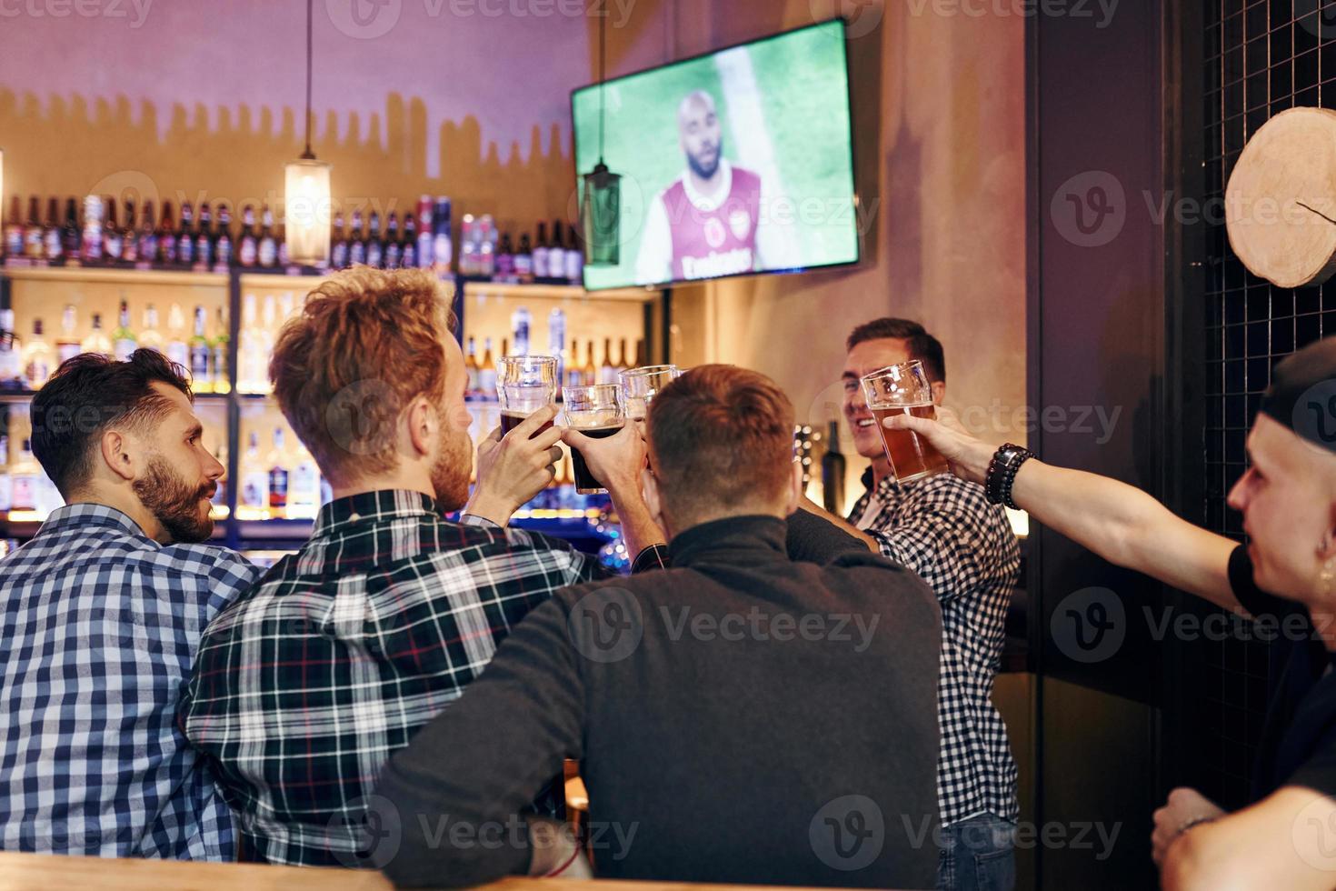 Cheering by knocking beer glasses. Group of people together indoors in the pub have fun at weekend time photo