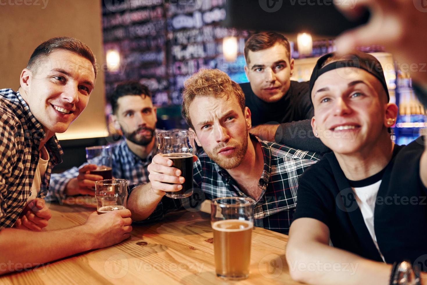 Man takes selfie by phone. Group of people together indoors in the pub have fun at weekend time photo