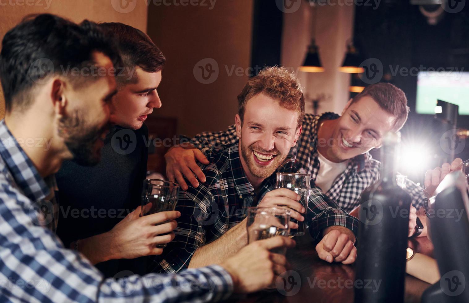 Cheering by knocking beer glasses. Group of people together indoors in the pub have fun at weekend time photo