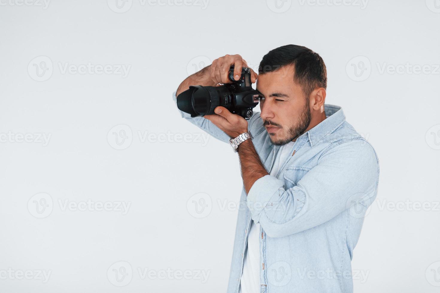 con cámara profesional. joven apuesto hombre de pie en el interior contra el fondo blanco foto