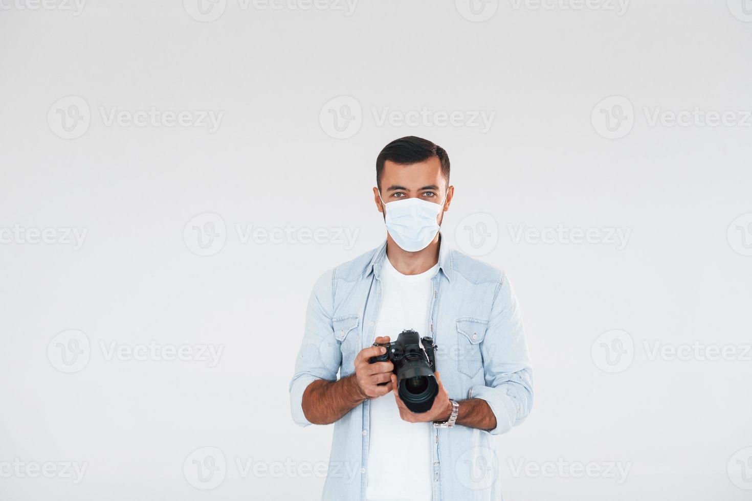 With professional camera. Young handsome man standing indoors against white background photo