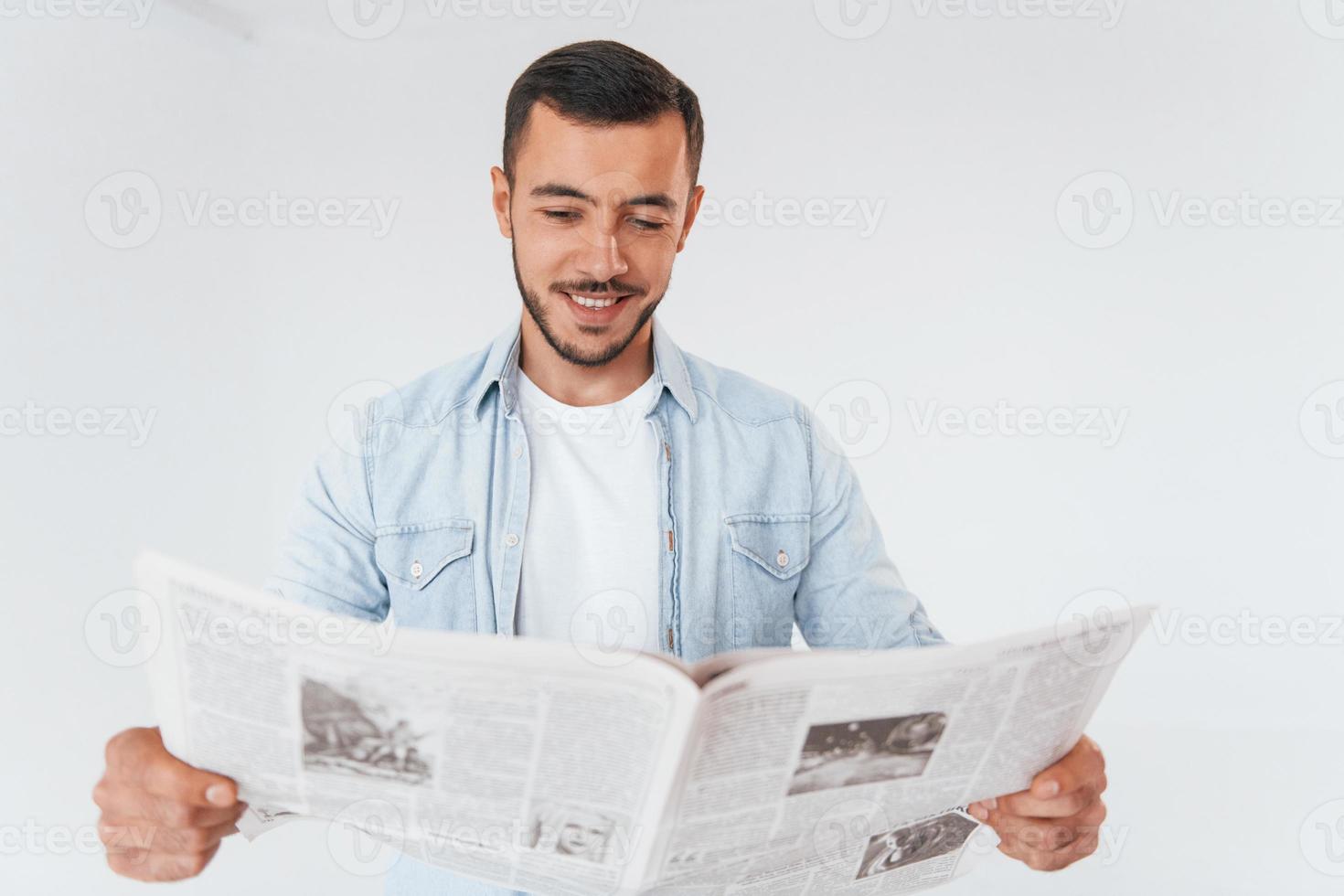Reads newspaper. Young handsome man standing indoors against white background photo