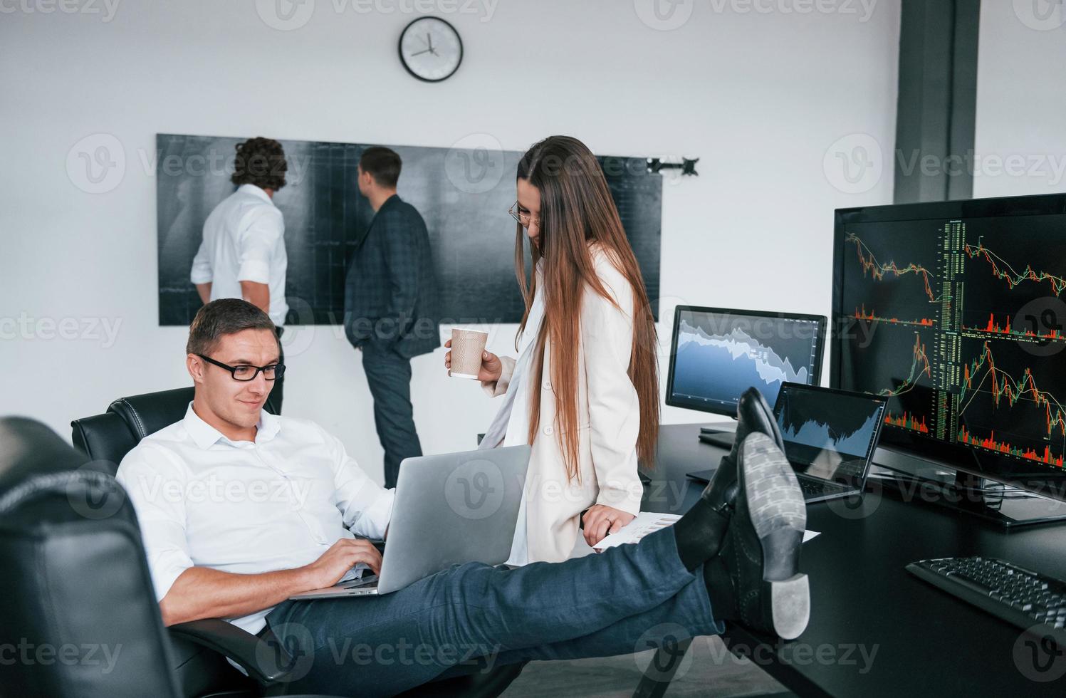 Woman and man have conversation. Team of stockbrokers works in modern office with many display screens photo