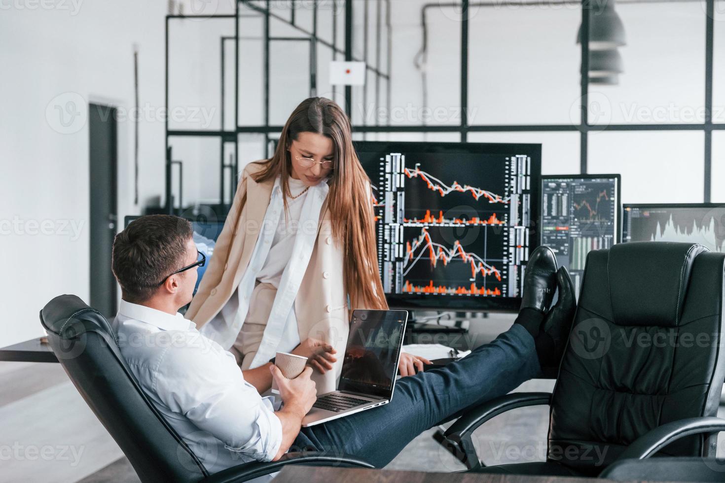 Woman and man have conversation. Team of stockbrokers works in modern office with many display screens photo