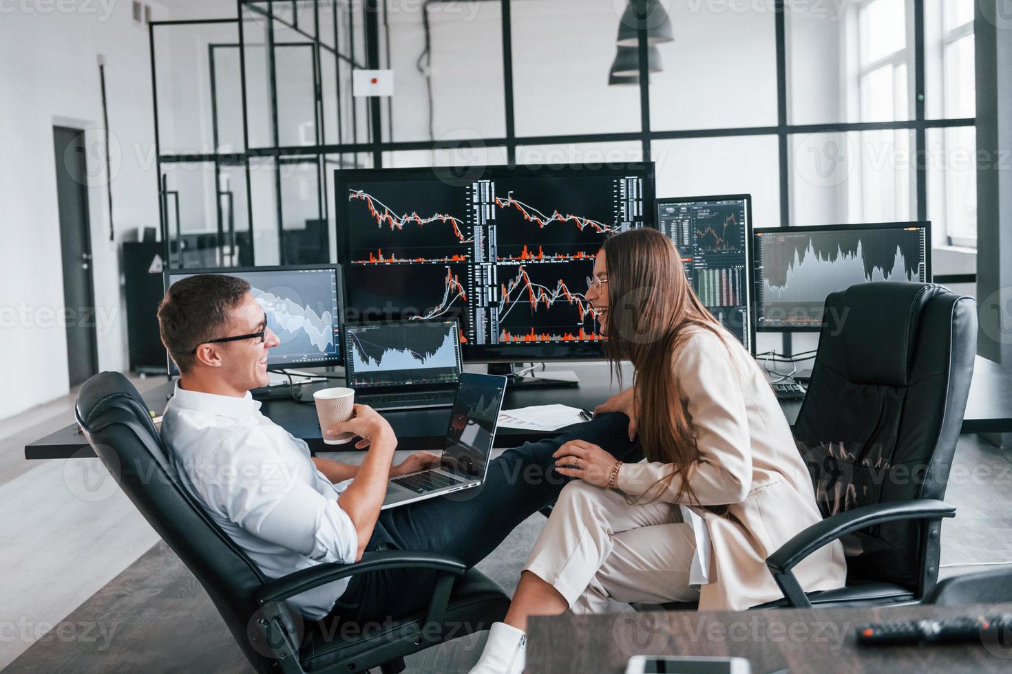 Woman and man have conversation. Team of stockbrokers works in modern office with many display screens photo