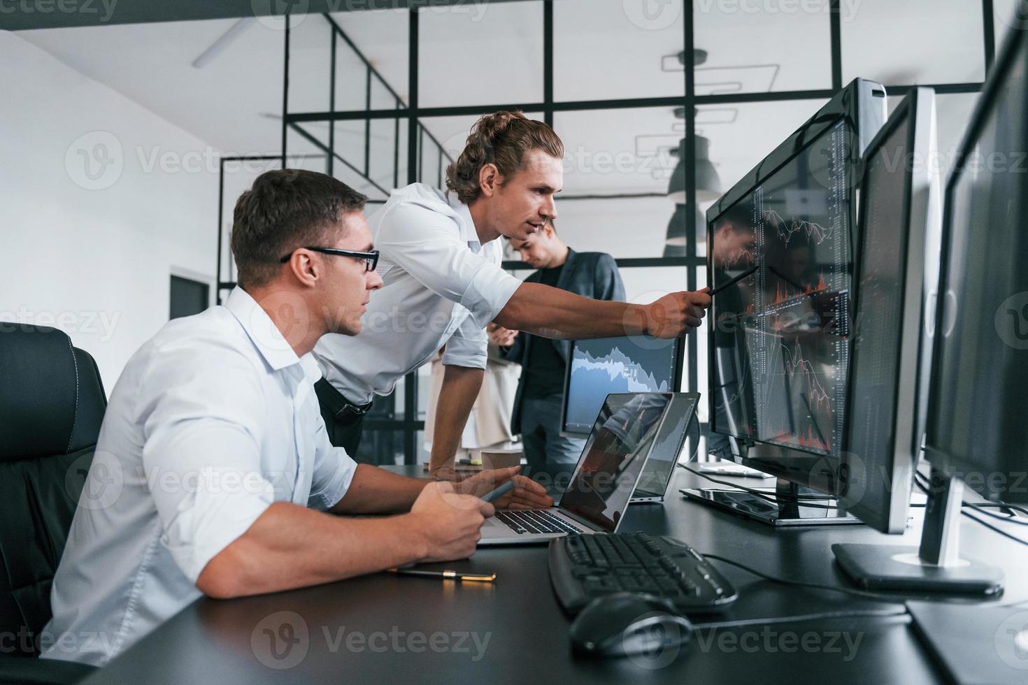 Guy in glasses concentrated at work. Team of stockbrokers is in modern office with many display screens photo