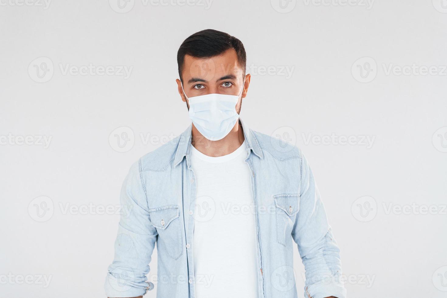 In protective mask. Young handsome man standing indoors against white background photo