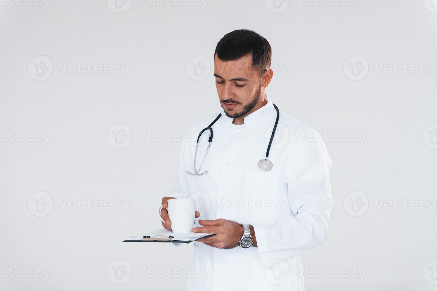 Medic in uniform. Young handsome man standing indoors against white background photo