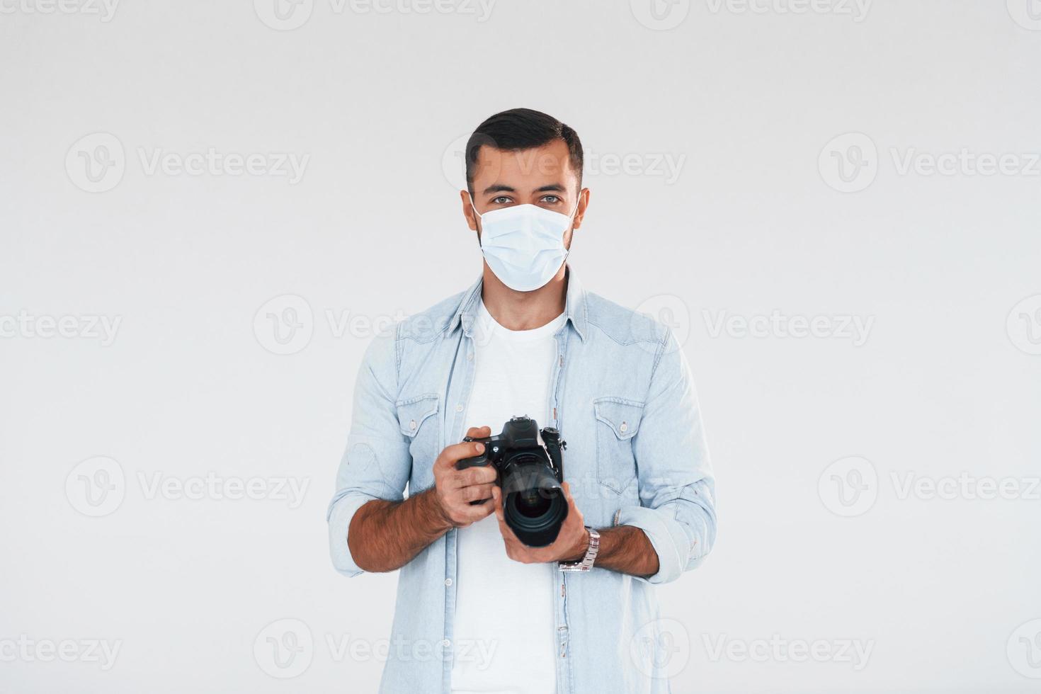 With professional camera. Young handsome man standing indoors against white background photo