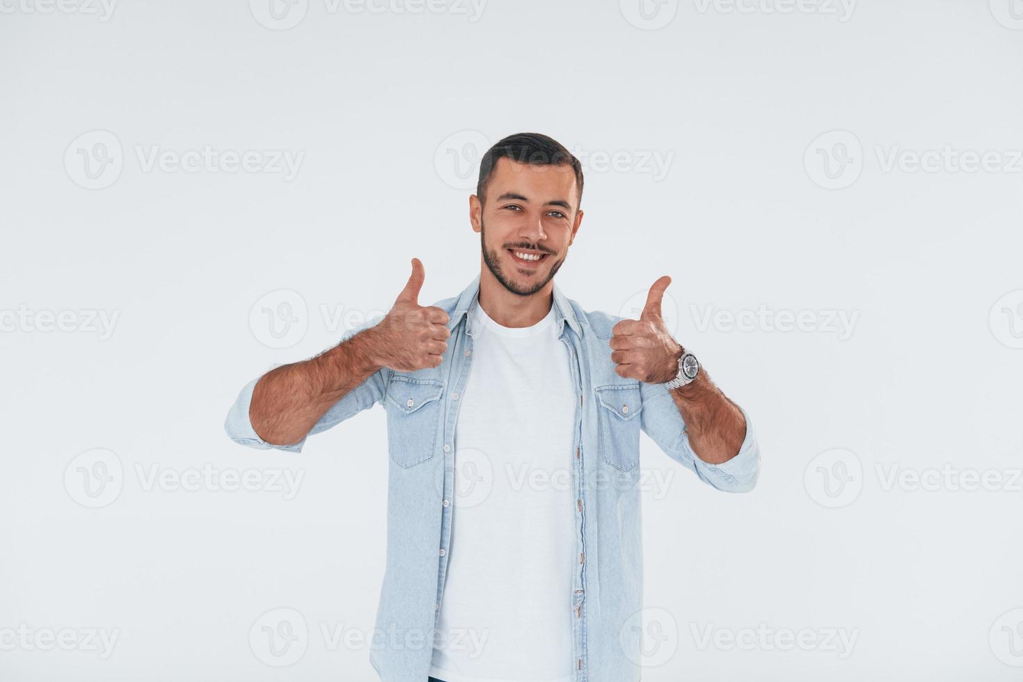 Thumbs up. Young handsome man standing indoors against white background photo