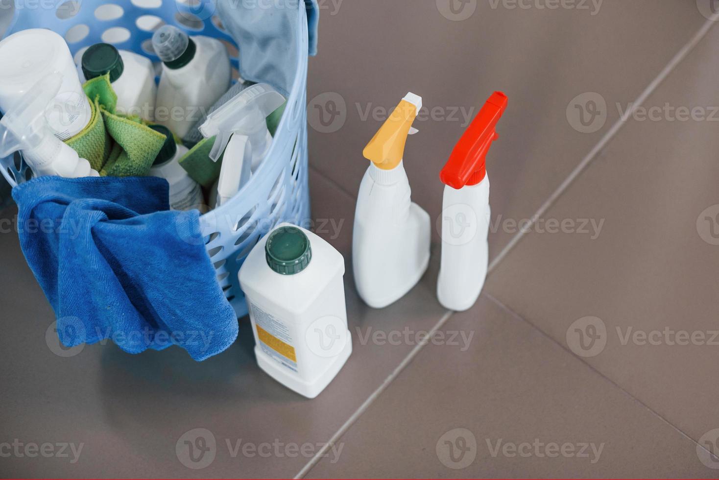 Close up view of bottles with detergent and basket indoors on the floor photo