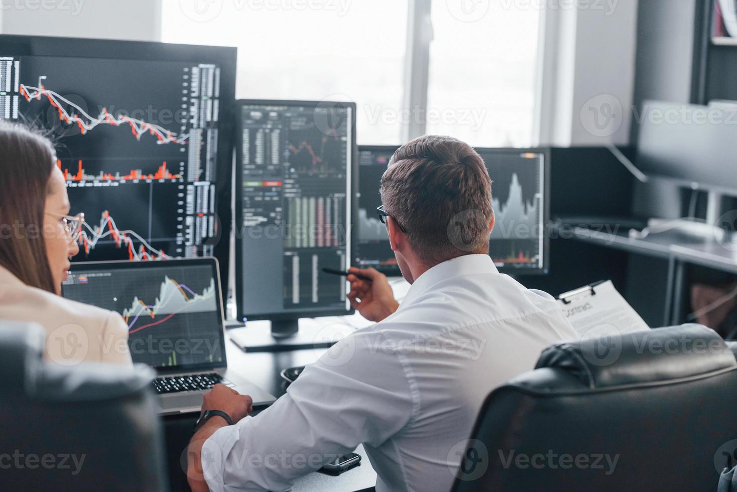 Team of stockbrokers works in modern office with many display screens photo