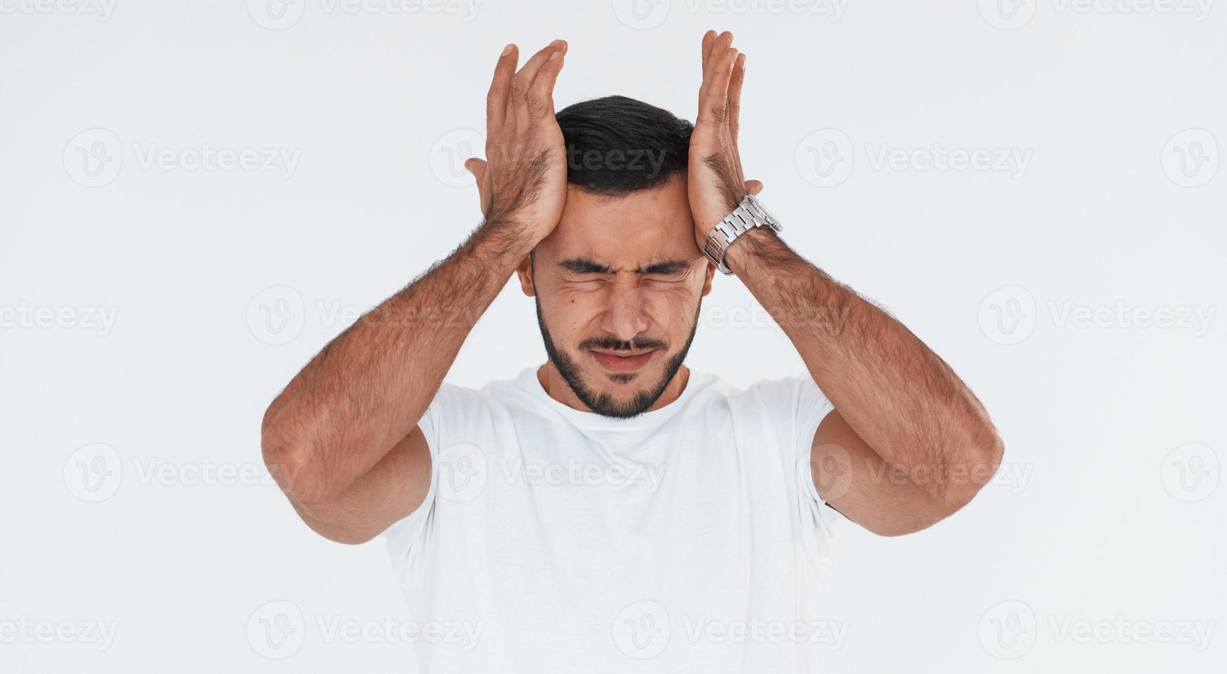 Feels headache. Young handsome man standing indoors against white background photo