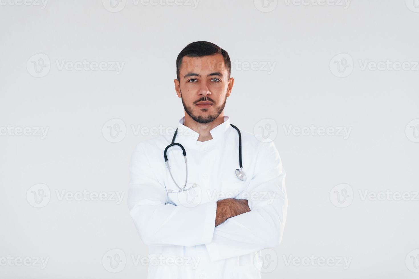 Medic in uniform. Young handsome man standing indoors against white background photo