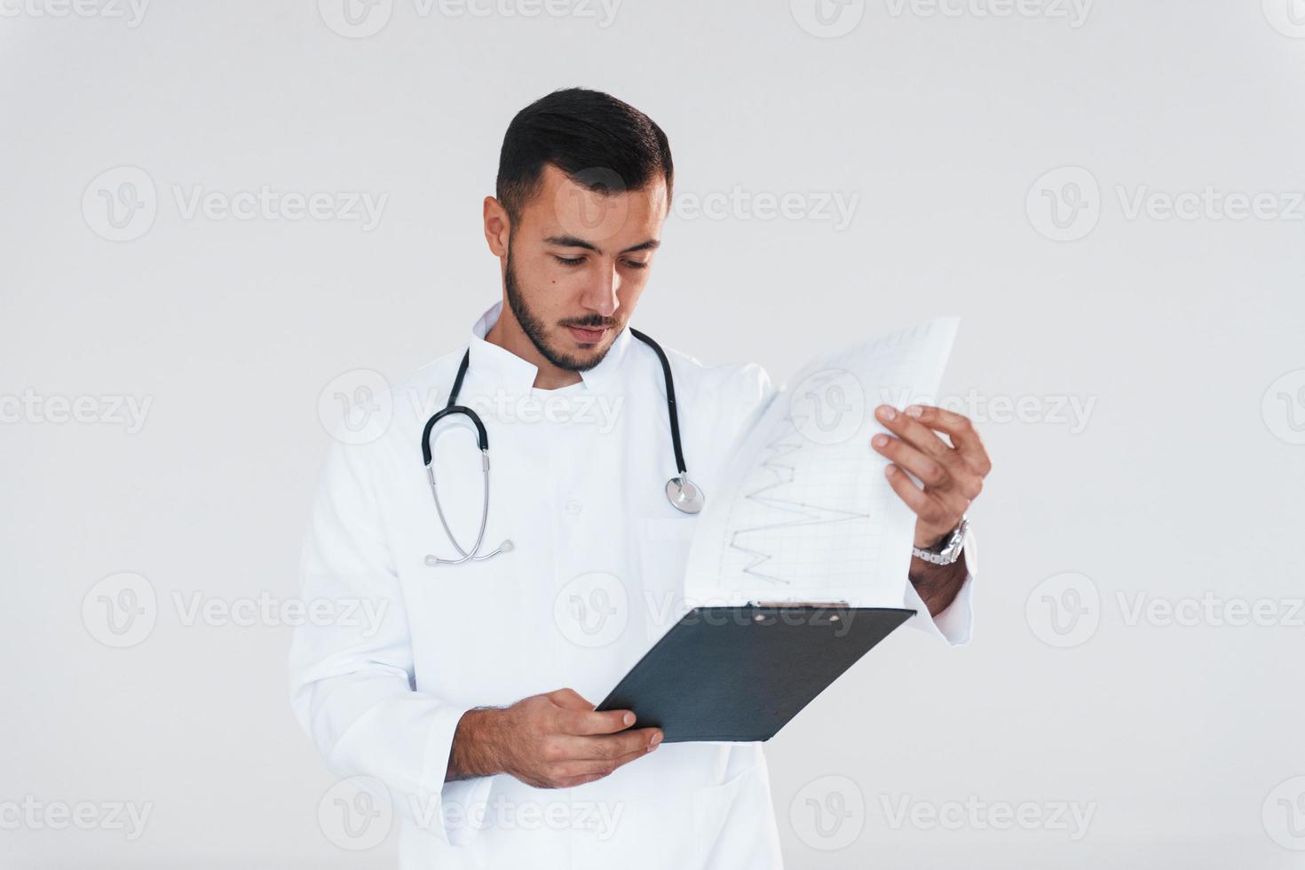 Medic in uniform. Young handsome man standing indoors against white background photo