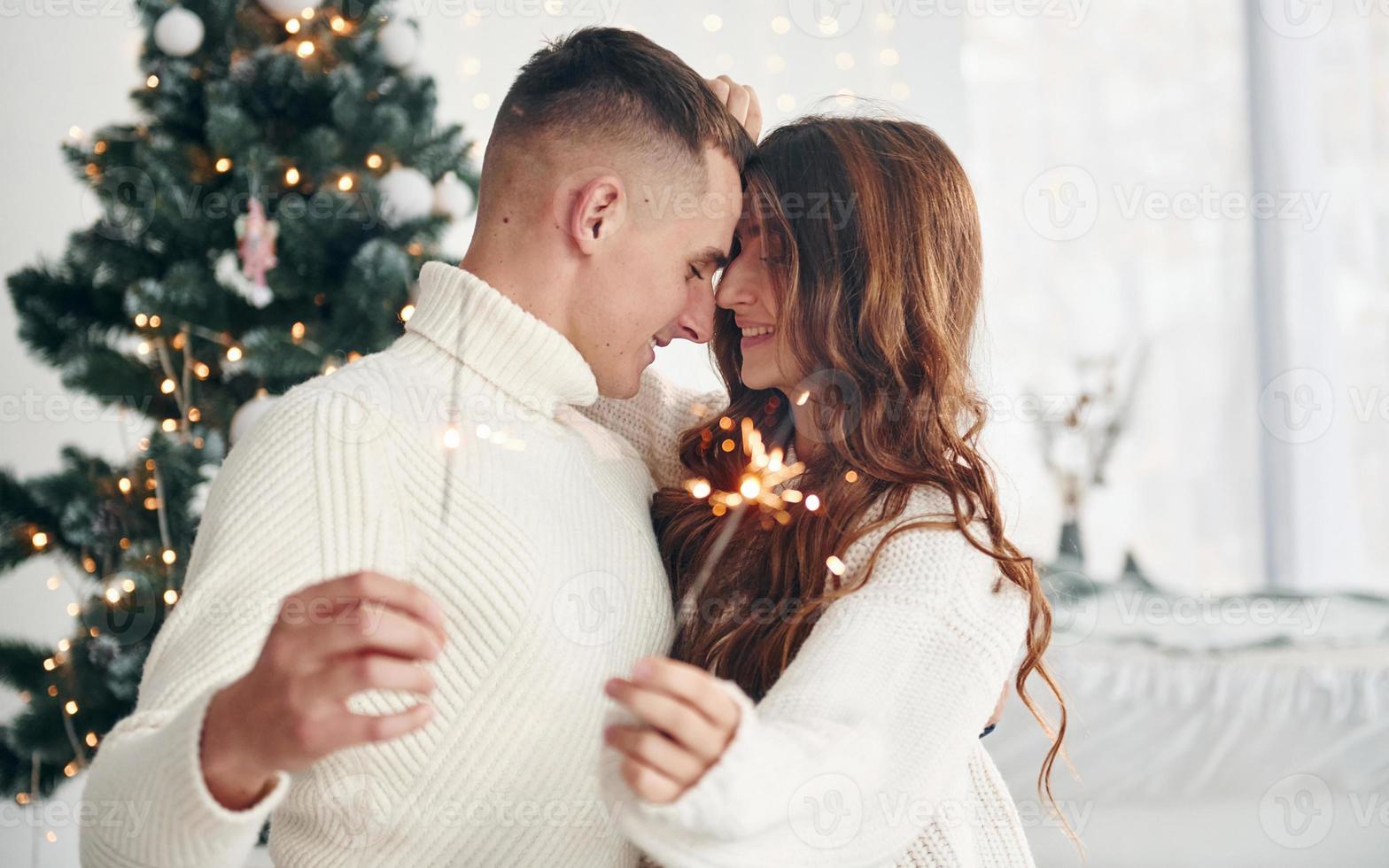 With sparklers in hands. Young romantic couple celebrates New year together indoors photo