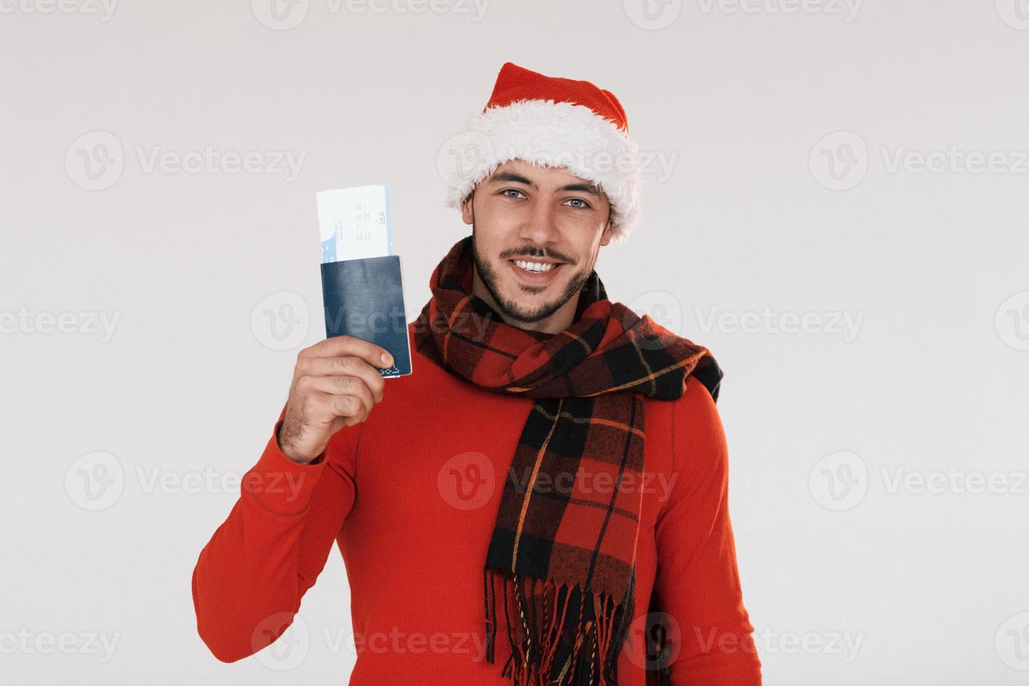 Holds airplane ticket. Young handsome man in New year clothes standing indoors against white background photo