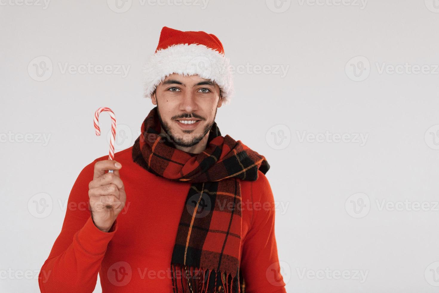 With candies. Young handsome man in New year clothes standing indoors against white background photo