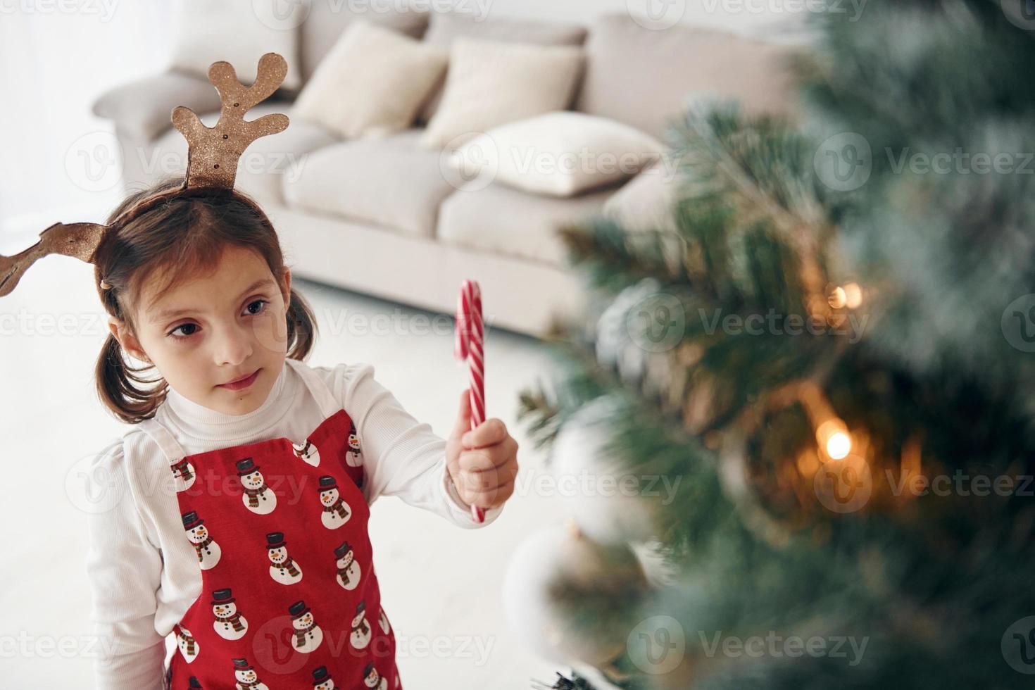 Cute little girl standing new New year tree with candy in hand photo