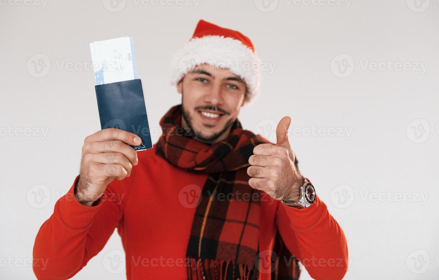 Holds airplane ticket. Young handsome man in New year clothes standing indoors against white background photo