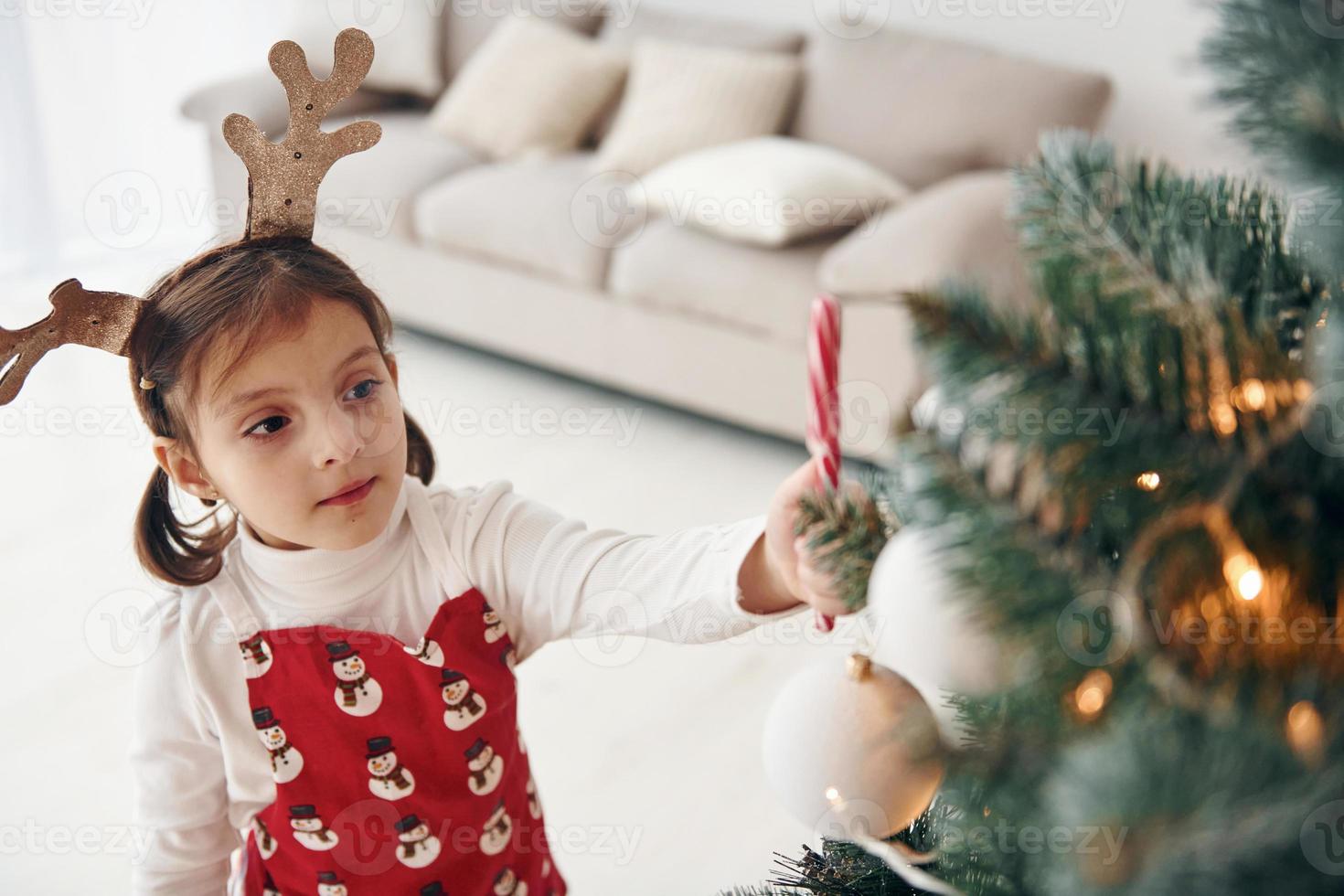 Cute little girl standing new New year tree with candy in hand photo