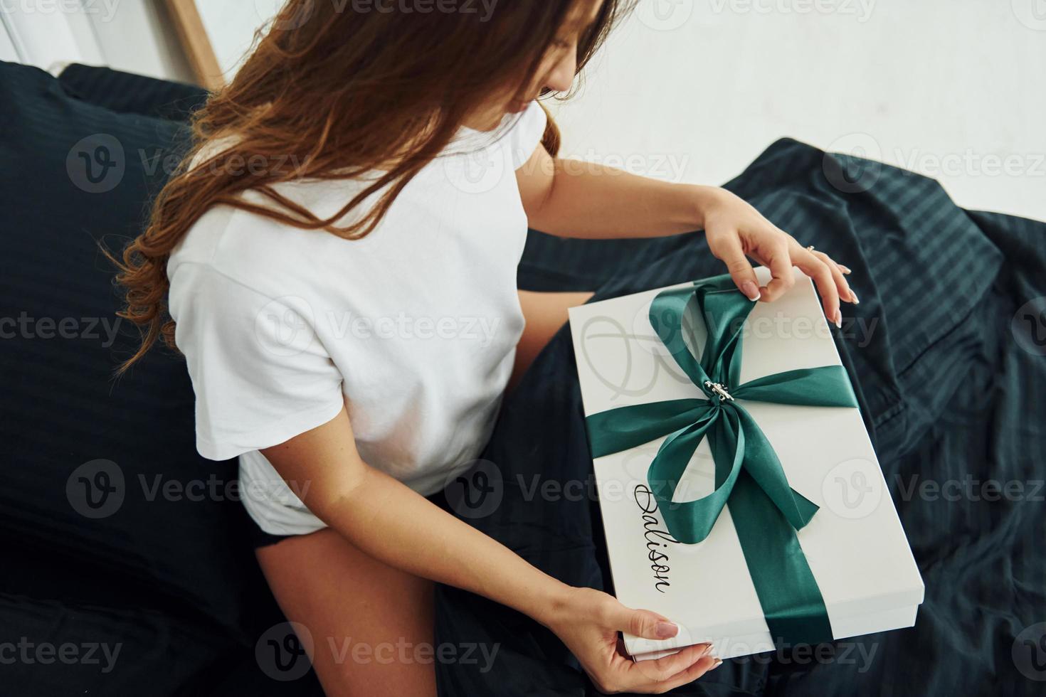 Gift box in hands of young woman. Interior and design of beautiful modern bedroom at daytime photo