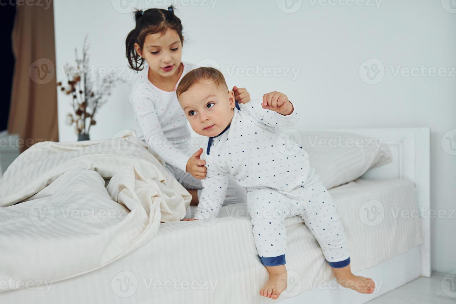 Two kids have fun while liyng down on bed. Interior and design of beautiful modern bedroom at daytime photo
