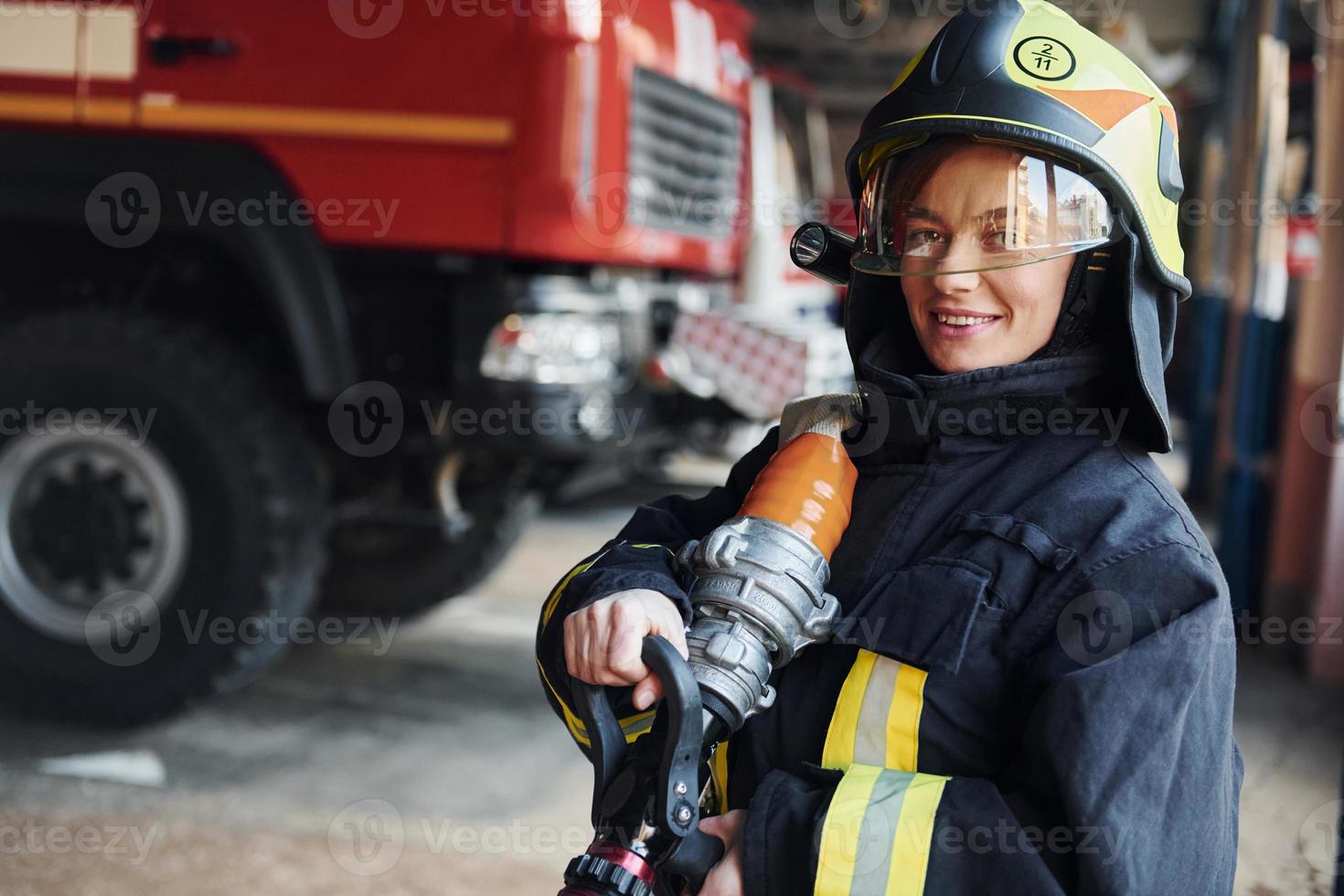 Hose in hands. Female firefighter in protective uniform standing near truck photo