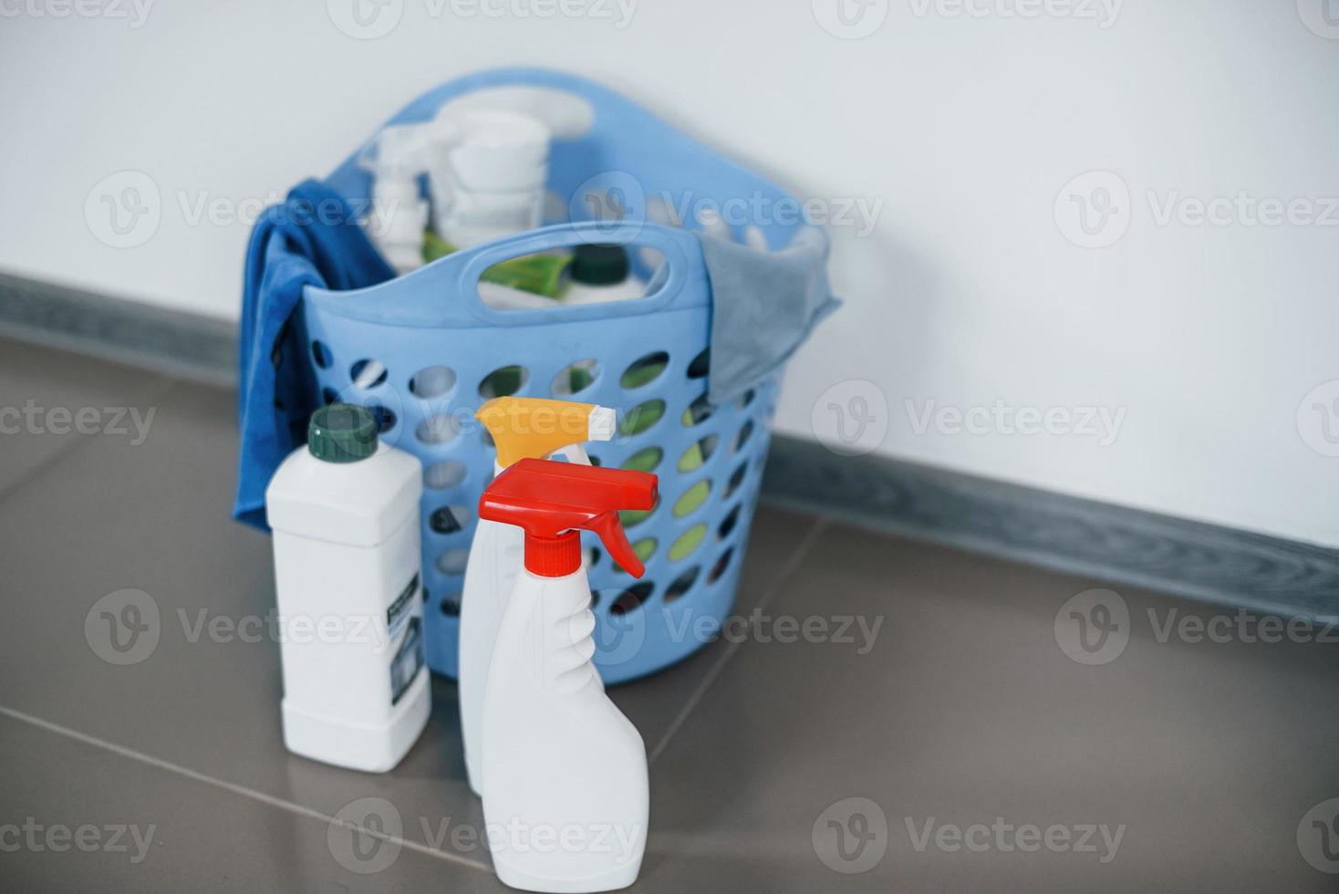 Close up view of bottles with detergent and basket indoors on the floor photo