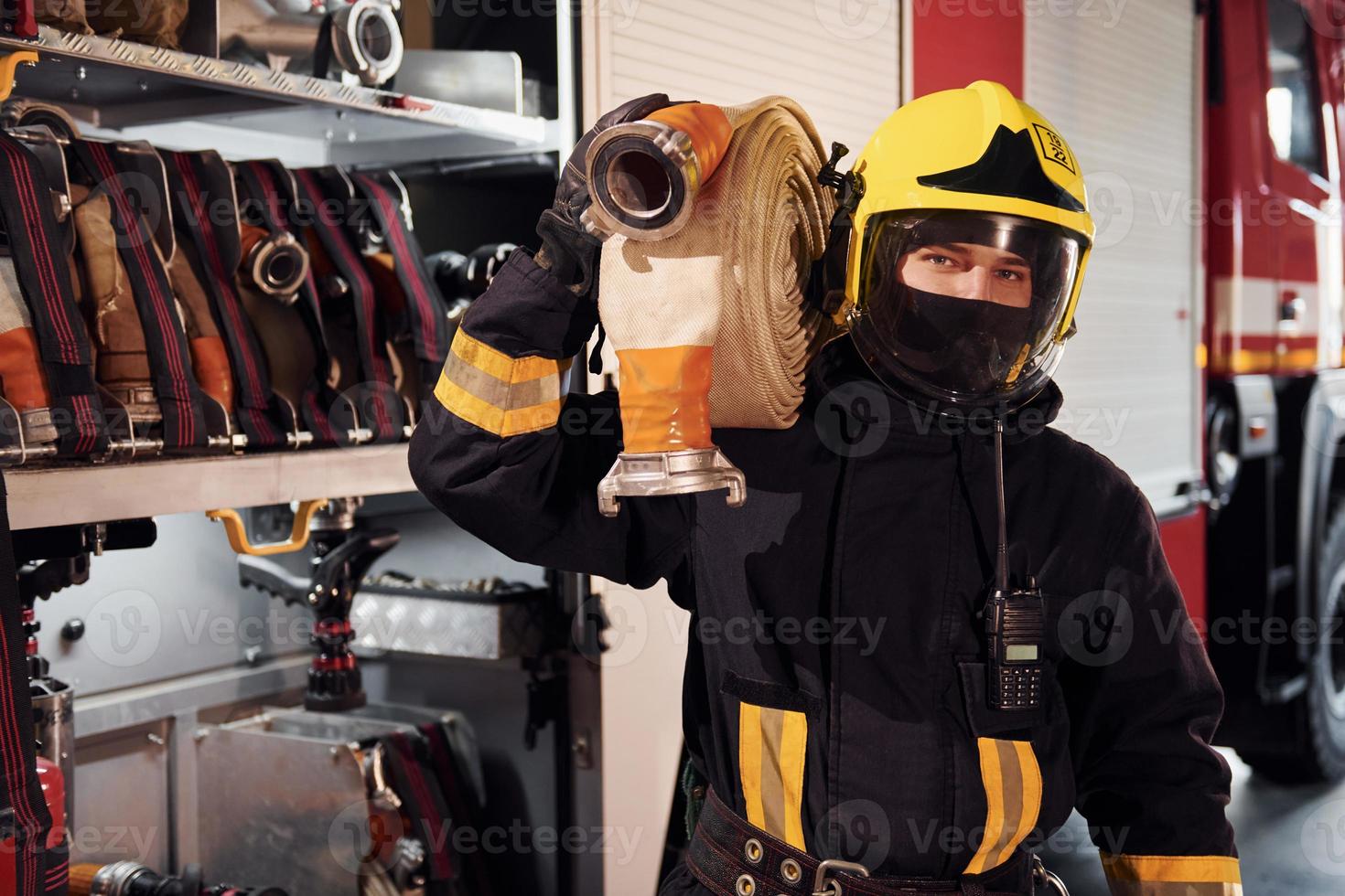 Holds hose. Male firefighter in protective uniform standing near truck photo