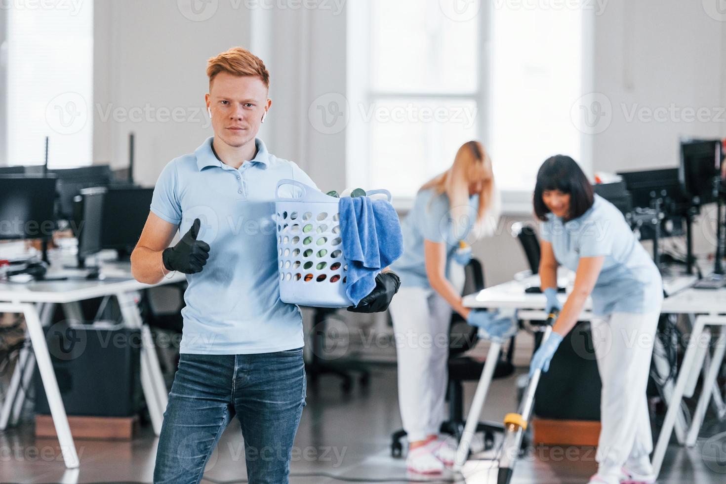 Man holds basket. Group of workers clean modern office together at daytime photo