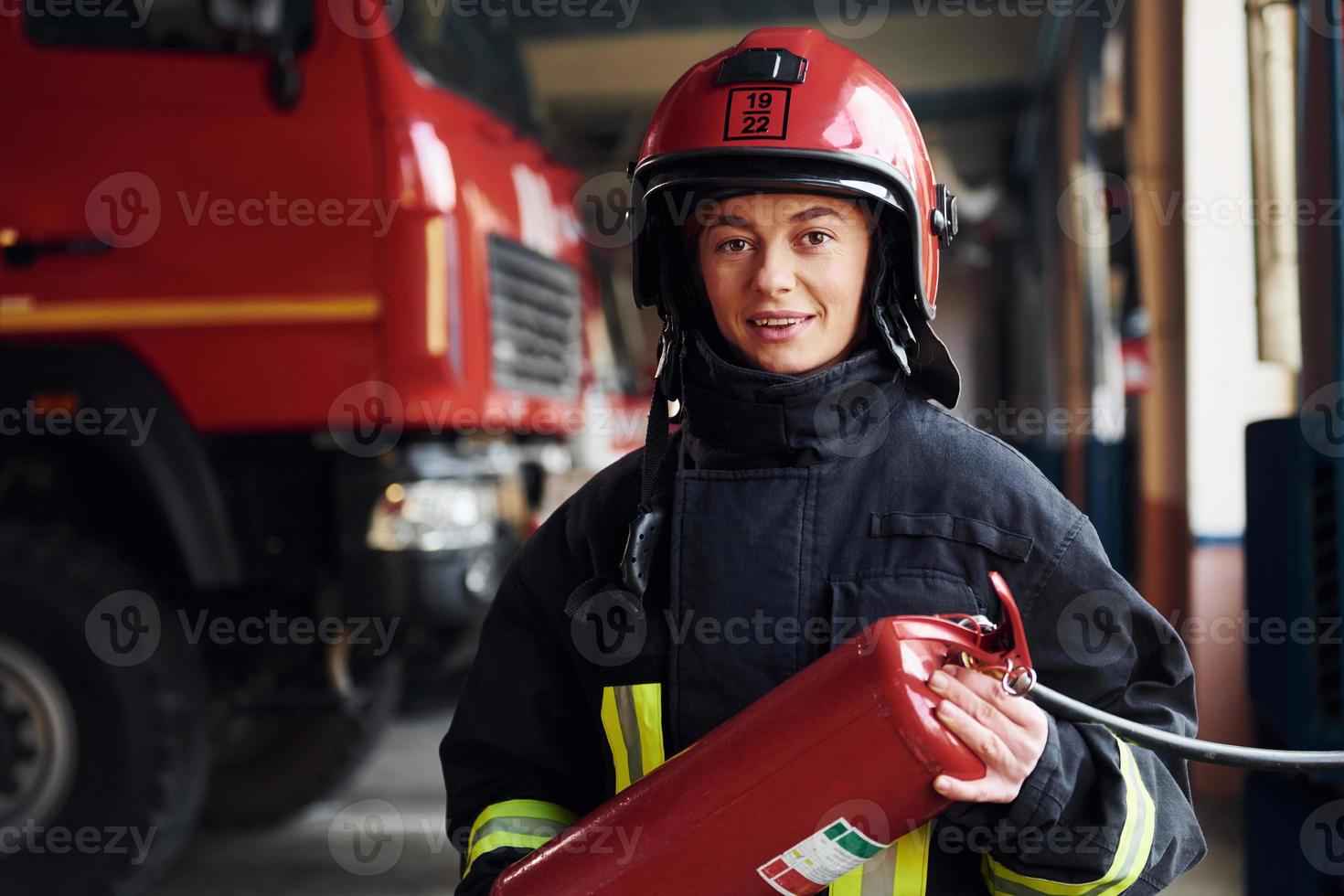 tiene extintor en las manos. bombero femenino en uniforme protector de pie cerca de camión foto