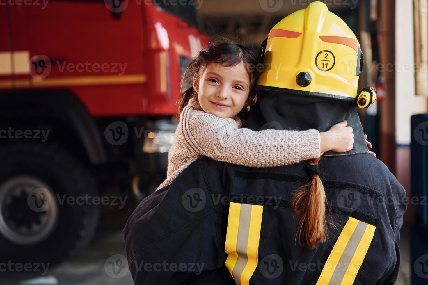 Happy little girl is with female firefighter in protective uniform photo