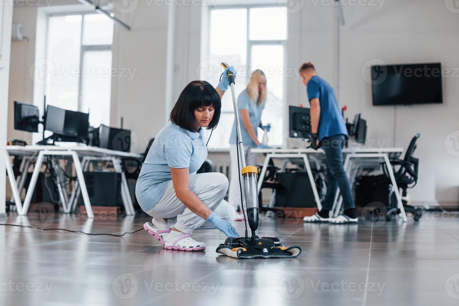 Woman uses vacuum cleaner. Group of workers clean modern office together at daytime photo