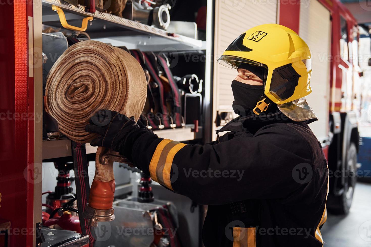 Holds hose. Male firefighter in protective uniform standing near truck photo