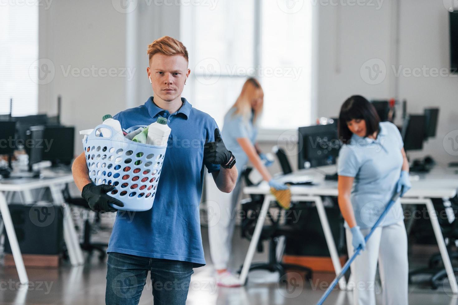 Man holds basket. Group of workers clean modern office together at daytime photo