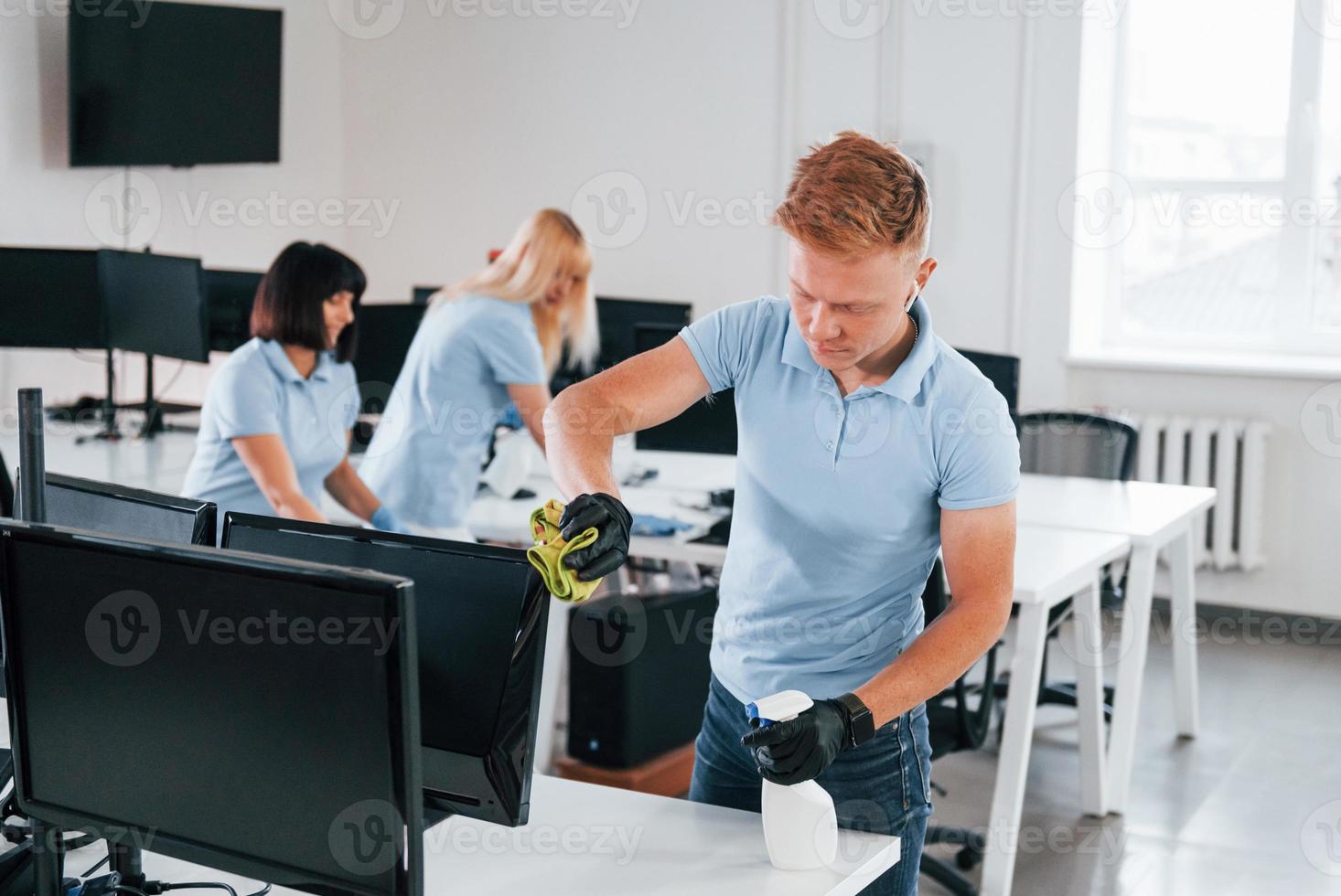 Cleans monitor. Group of workers clean modern office together at daytime photo