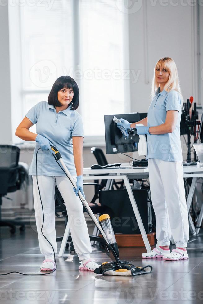 Woman uses vacuum cleaner. Group of workers clean modern office together at daytime photo