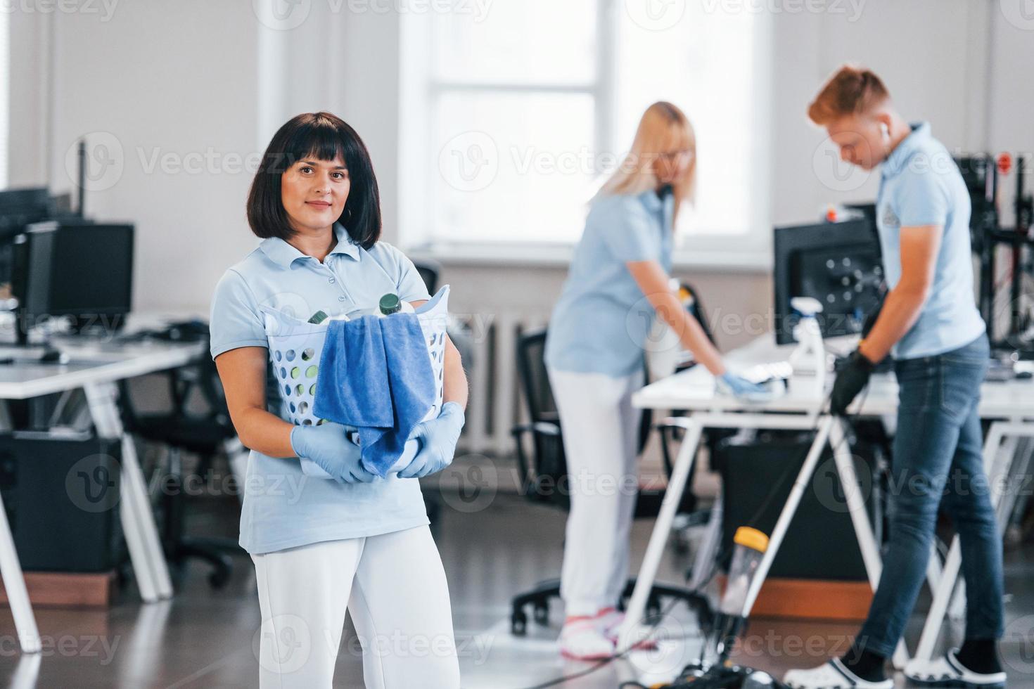 Woman with basket. Group of workers clean modern office together at daytime photo