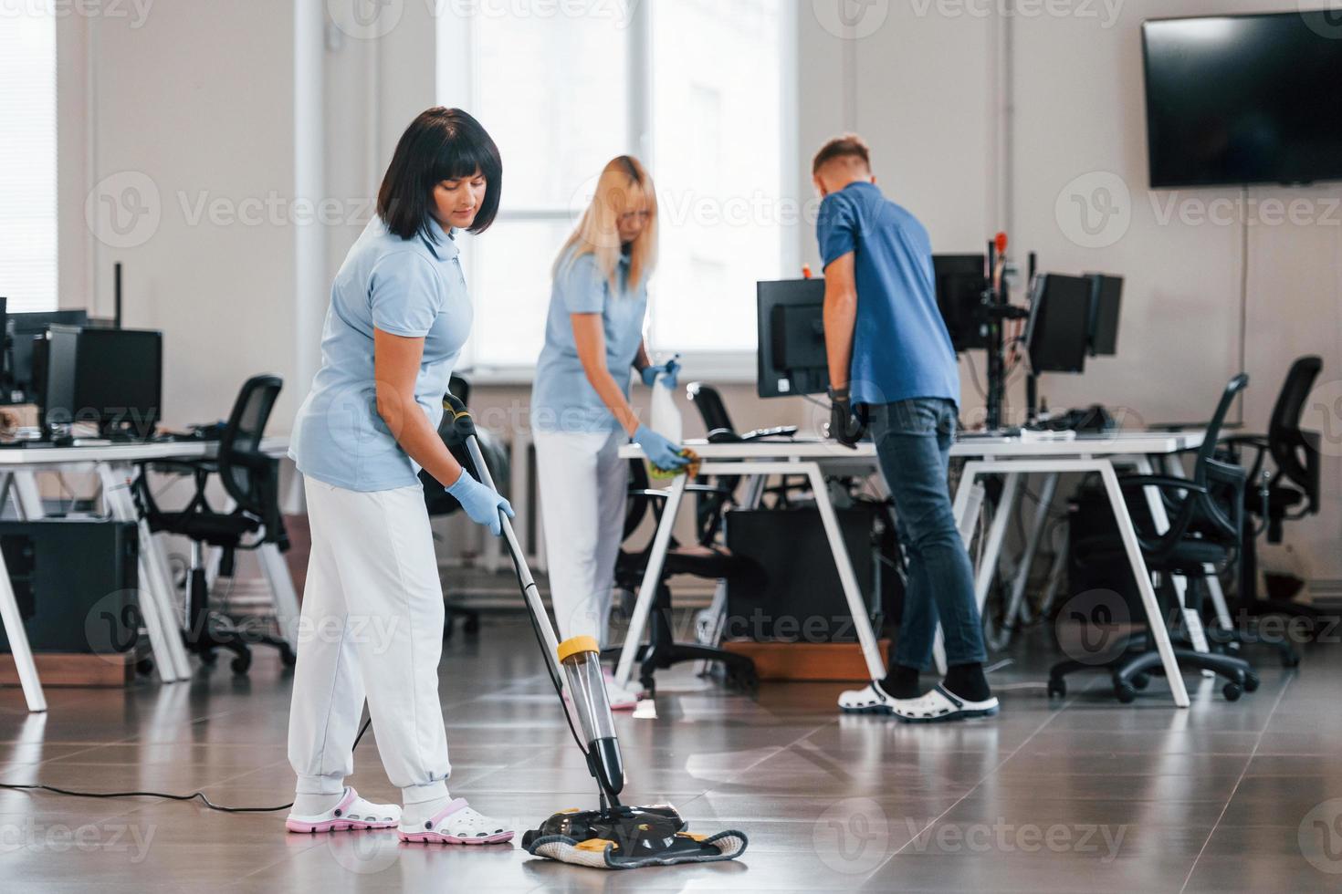 Woman uses vacuum cleaner. Group of workers clean modern office