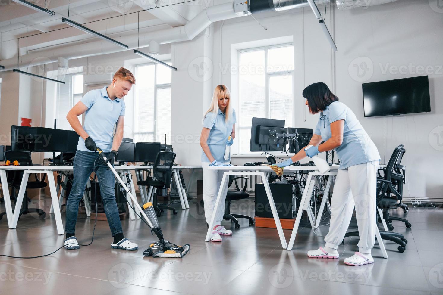 Cleans floor. Group of workers clean modern office together at daytime photo