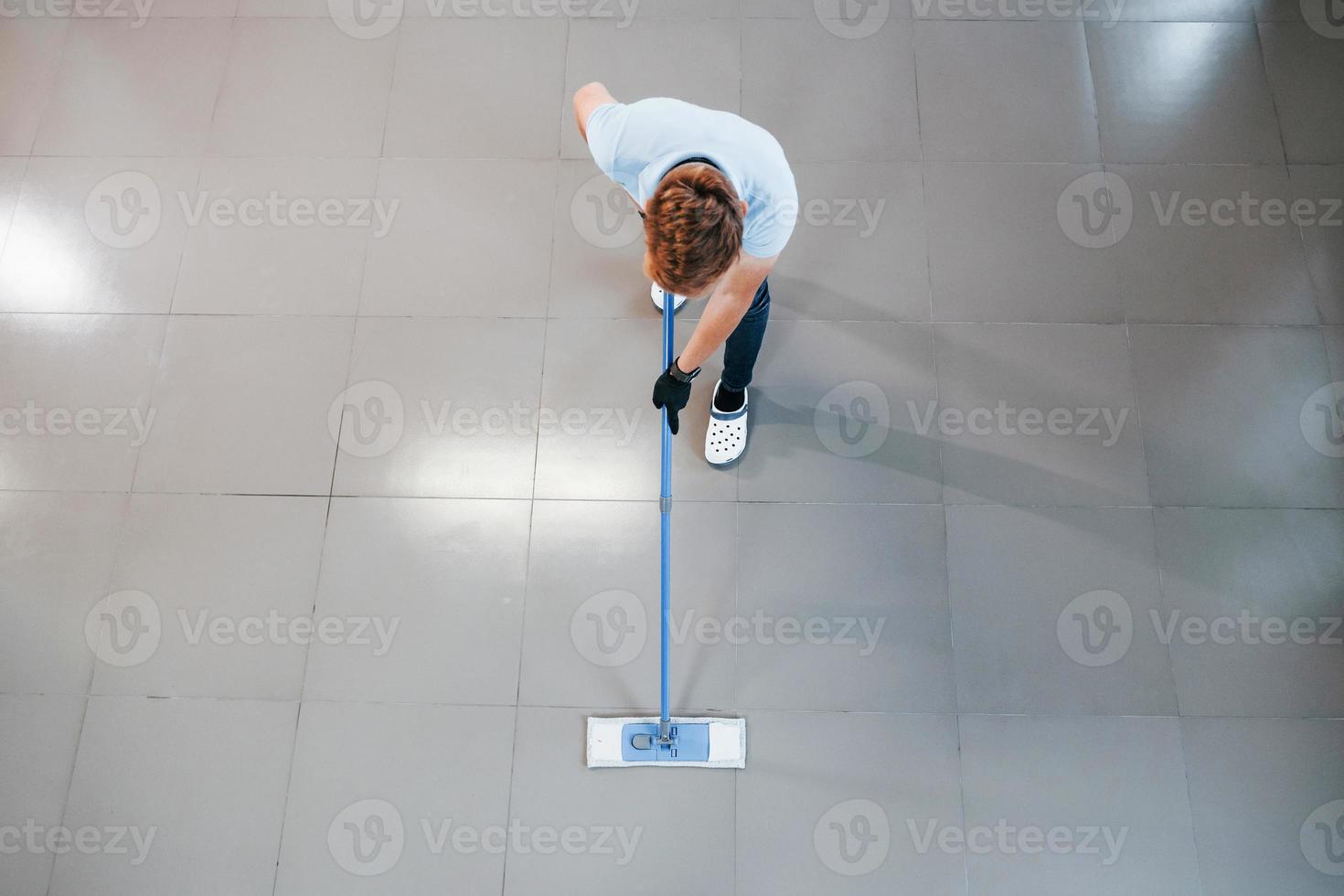 Top view of man in blue shirt and protective gloves that uses vacuum cleaner photo